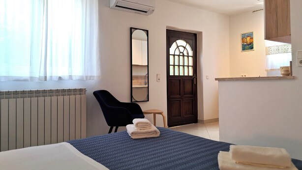 Habitación de hotel con cama, una silla, una mesita, un espejo y una puerta con ventana.