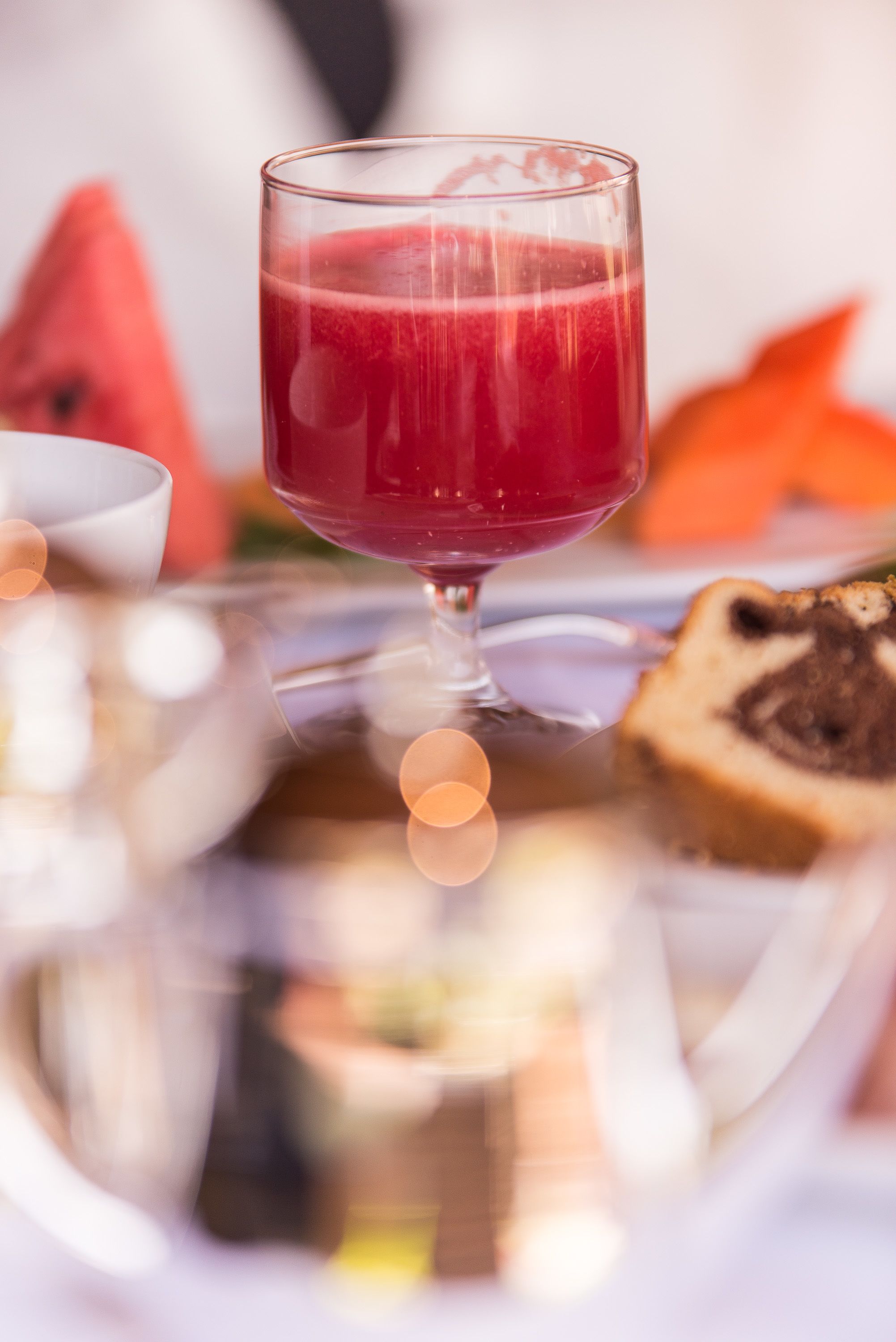 A glass of red beverage on a tray with a slice of cake and a bowl.