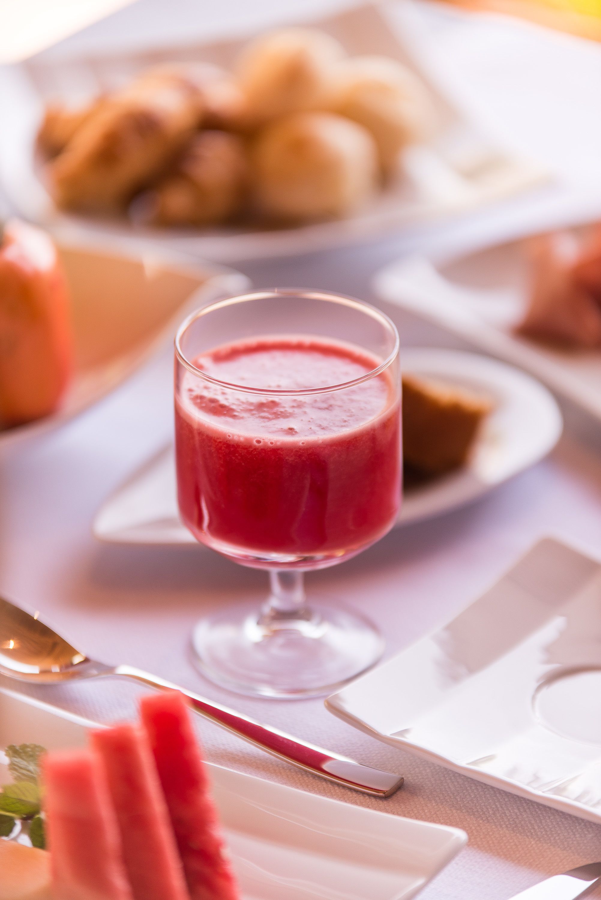 Uma mesa posta com um copo de bebida vermelha, pratos de comida e talheres.