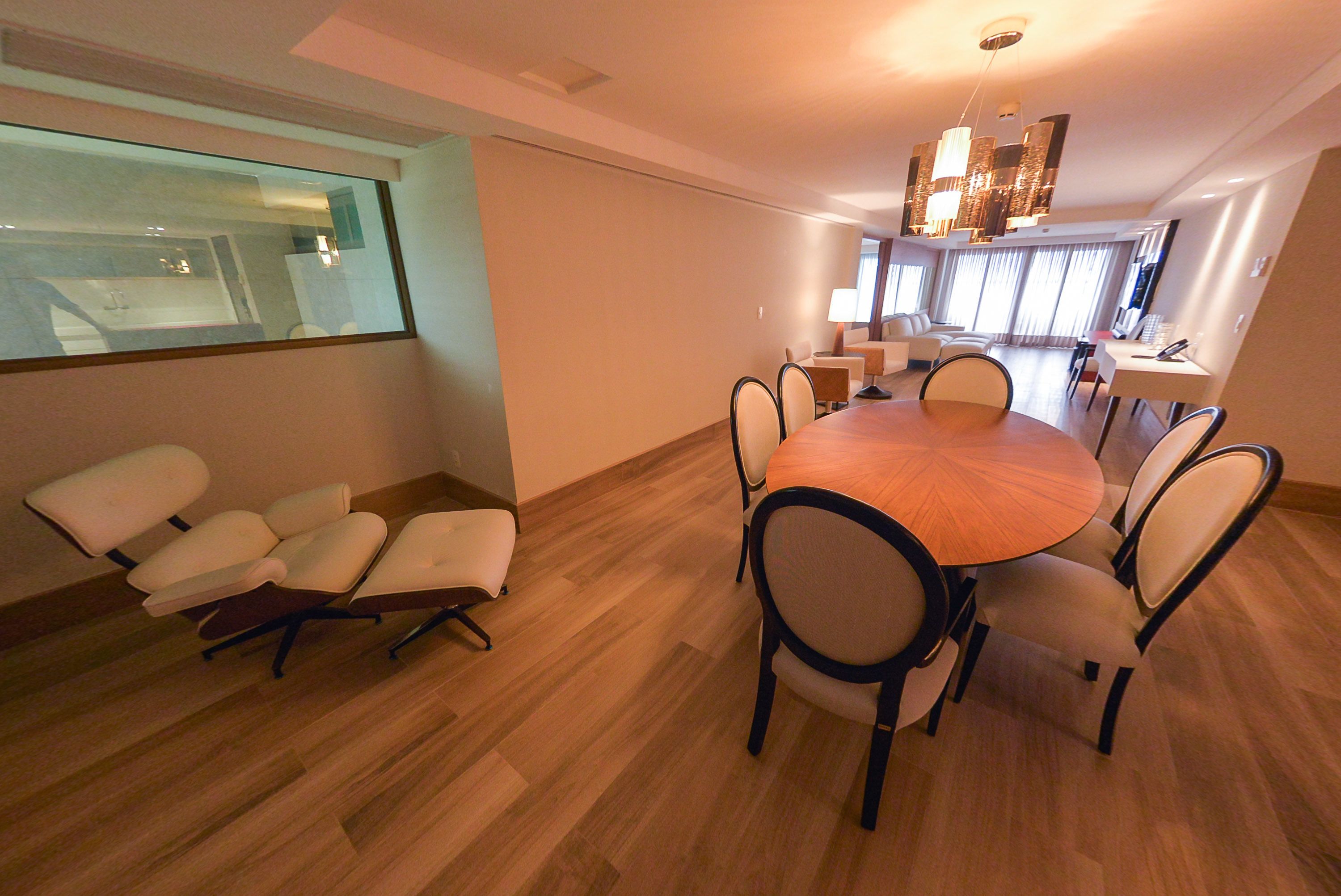 A modern dining area with a round table and chairs, a glass partition, and a view of a kitchen.