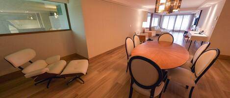 A modern dining area with a round table and chairs, a glass partition, and a view of a kitchen.