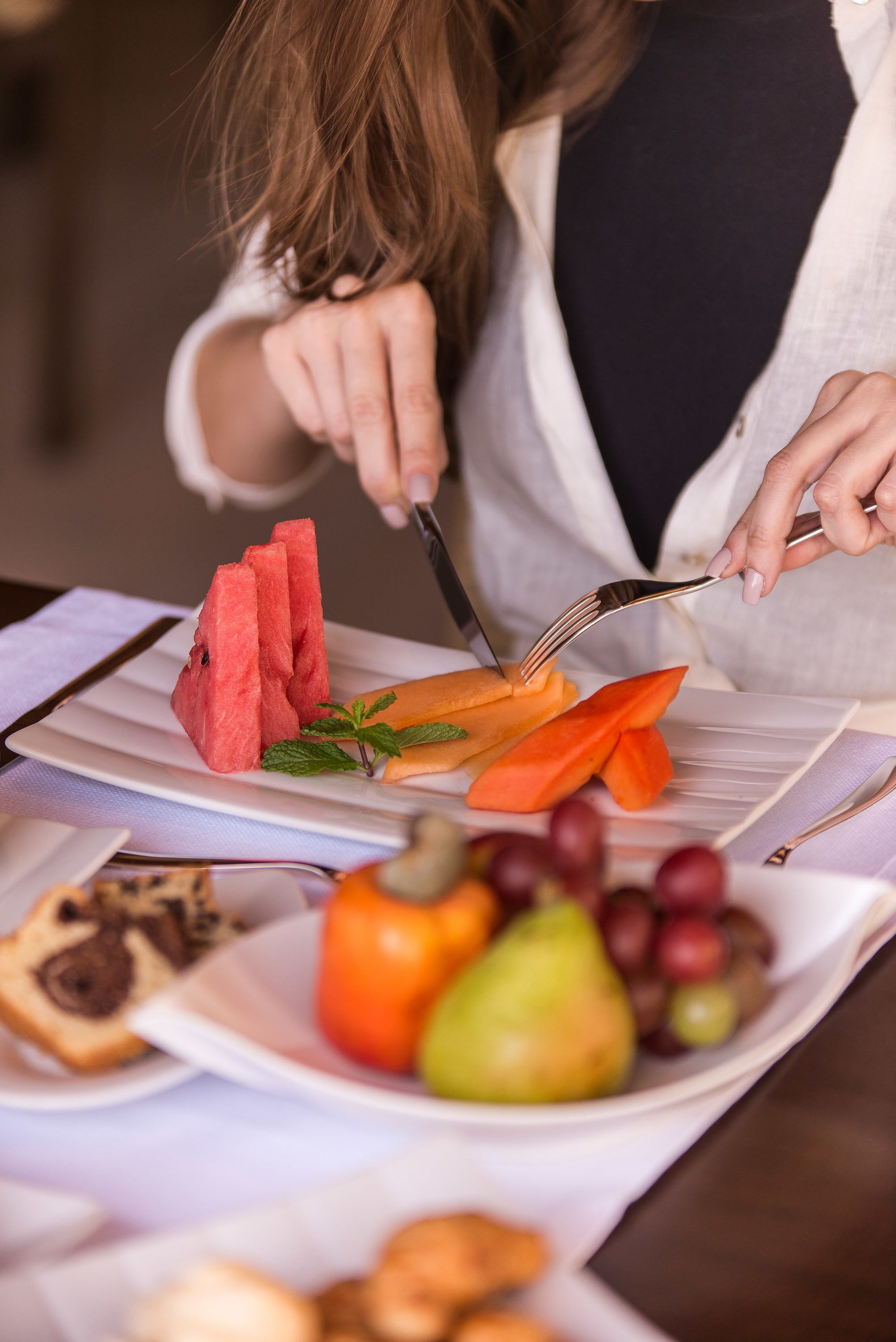 A person cutting watermelon and carrot on a white plate.