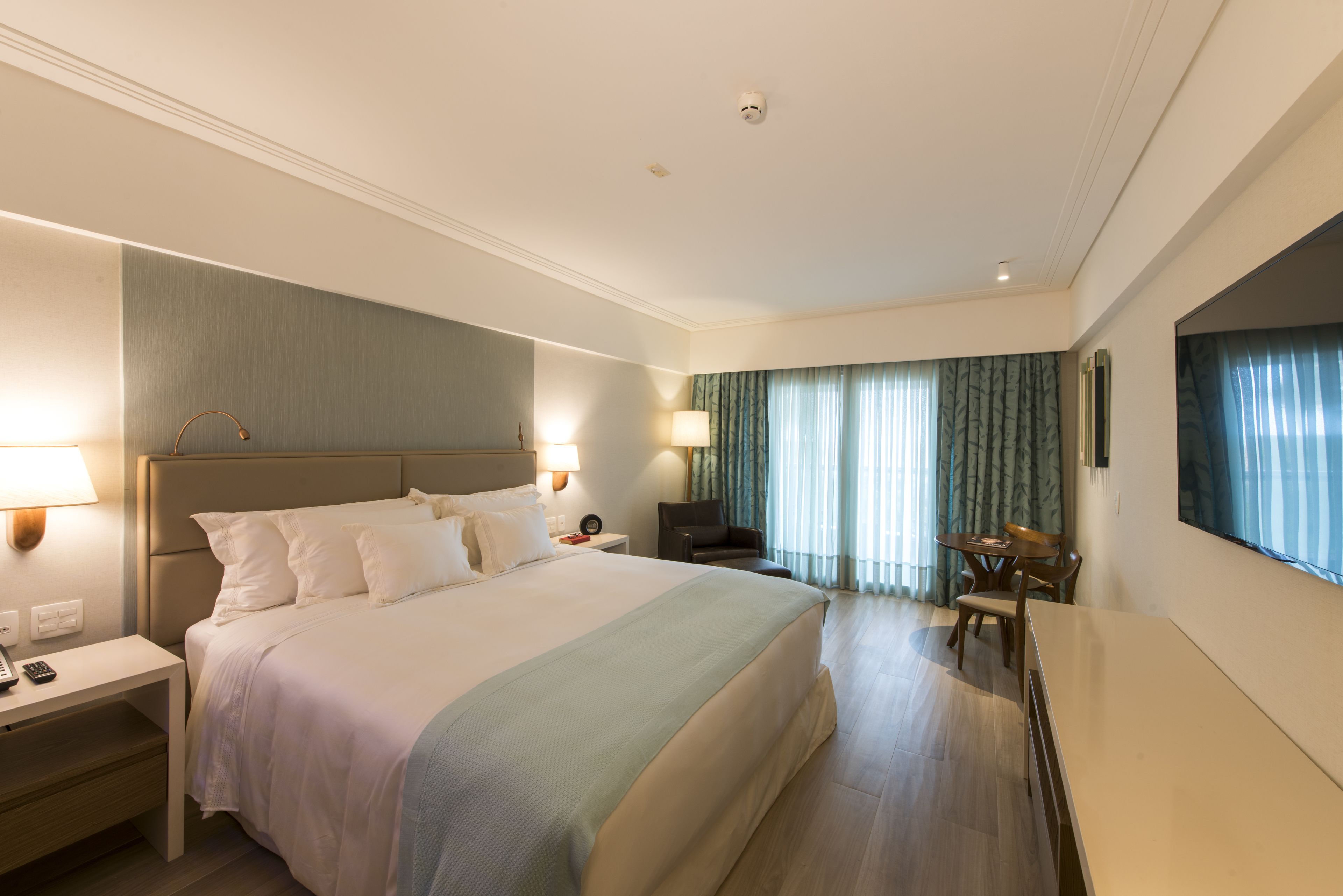 A hotel room with a large bed, bedside tables, a desk, and a chair.