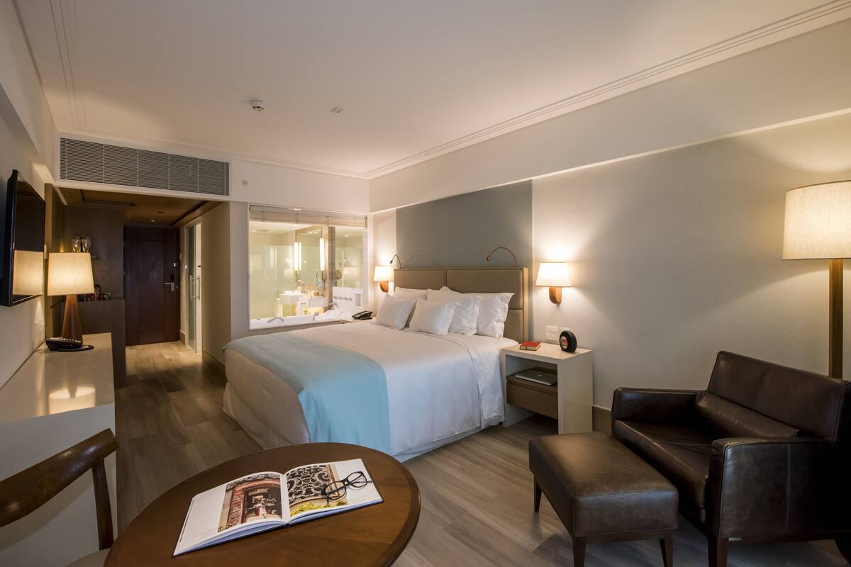 Habitación de hotel con cama, mesitas de noche, sofá, mesa de lectura y televisión.