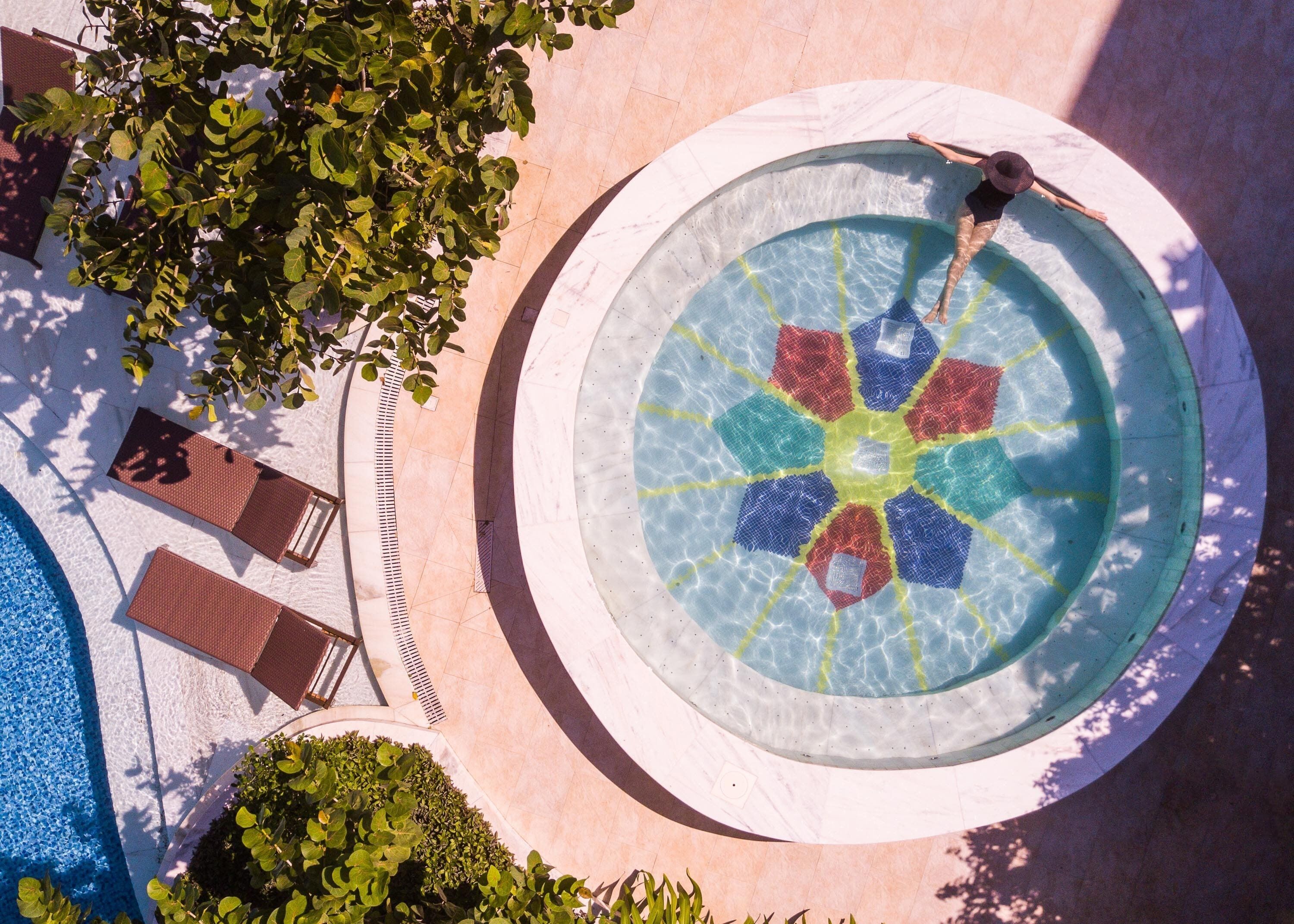 An outdoor swimming pool with a circular design, surrounded by a tiled area with lounge chairs and a small garden.