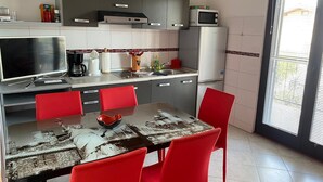 A modern kitchen with a dining table, red chairs, a flat-screen TV, and a refrigerator. - Apartments Marlina (Rovinj)