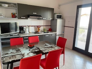 Una cocina moderna con una mesa de comedor, sillas rojas, un televisor de pantalla plana y un refrigerador.