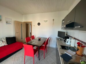 A compact living space with a dining table, red chairs, a sofa, a kitchen area with a stove, and a television. - Apartments Marlina (Rovinj)