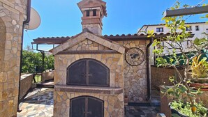 A stone-built outdoor kitchen with a clock, surrounded by potted plants and a tiled patio. - Apartments Marlina (Rovinj)