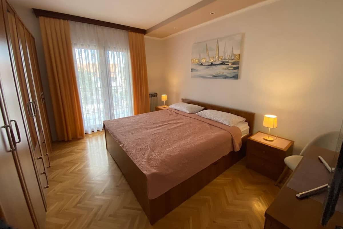 Une chambre avec un grand lit, un plancher en bois, un tableau au mur et un bureau avec une lampe.