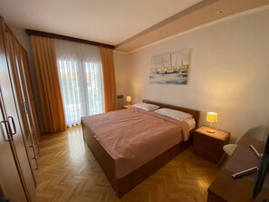 A bedroom with a large bed, wooden floor, a painting on the wall, and a desk with a lamp. - Apartments Marlina (Rovinj)