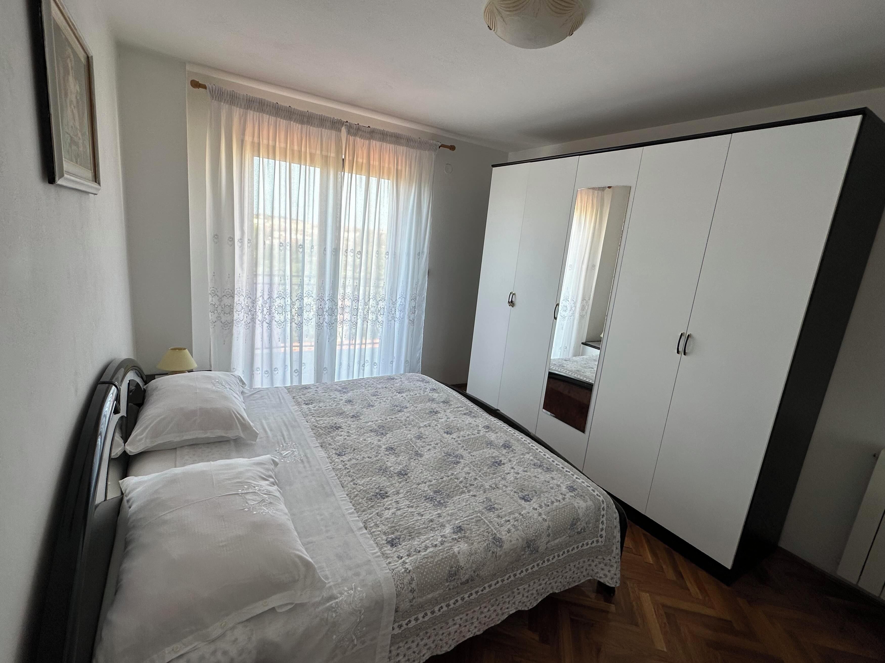 A bedroom with a bed, a wardrobe, a mirror, and a window with curtains.