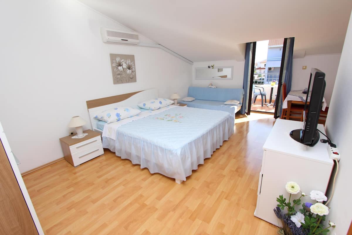 Une chambre à coucher comprenant un lit, des tables de chevet, un bureau avec une chaise, une télévision et une fenêtre avec des rideaux.