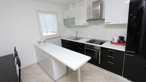 Een moderne keuken met een wit aanrecht, zwarte kastjes, een roestvrijstalen afzuigkap en een raam met zonwering.