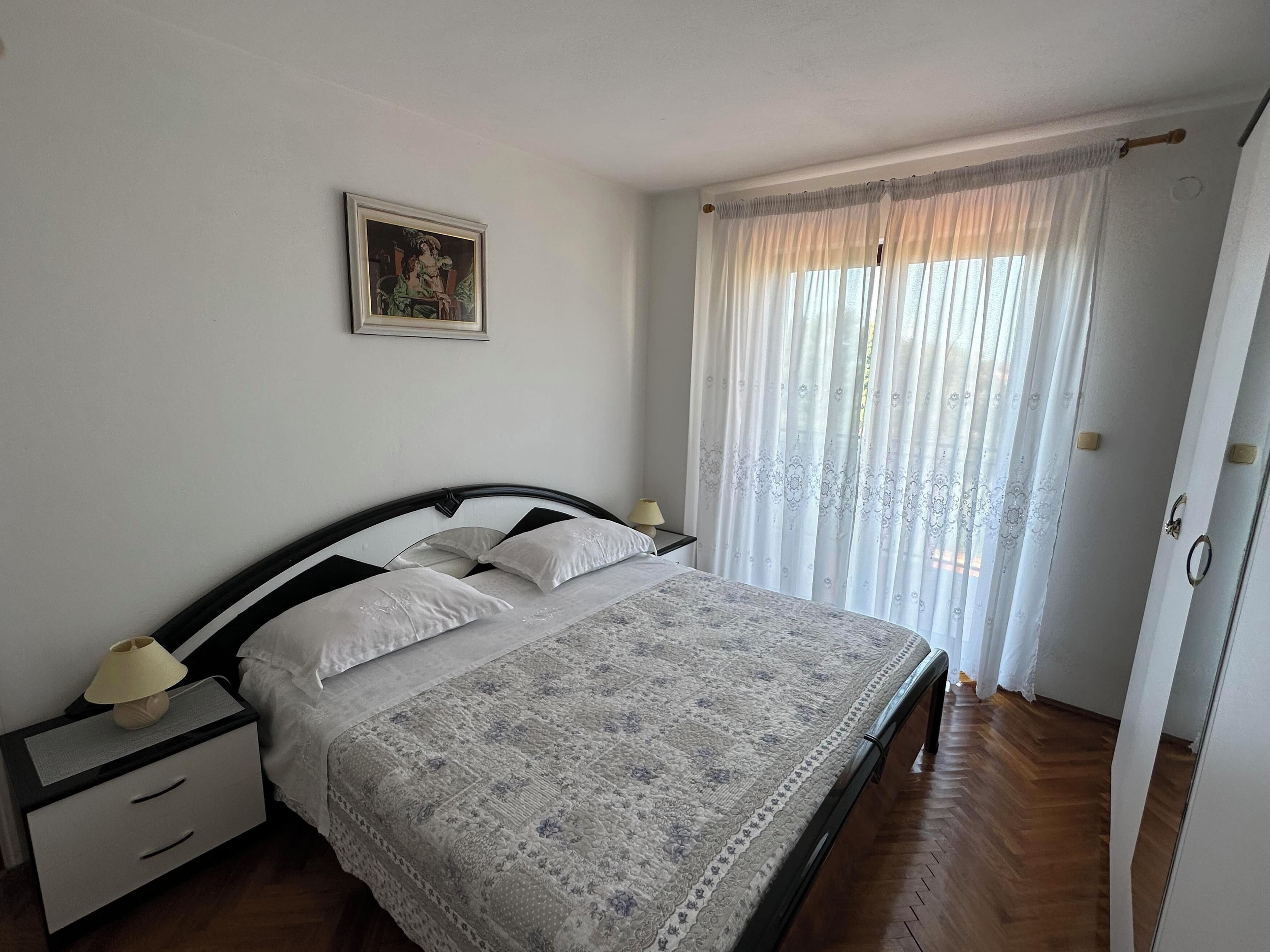 Une chambre à coucher avec un lit, des tables de chevet, une lampe, un tableau encadré au mur et une fenêtre avec des rideaux.
