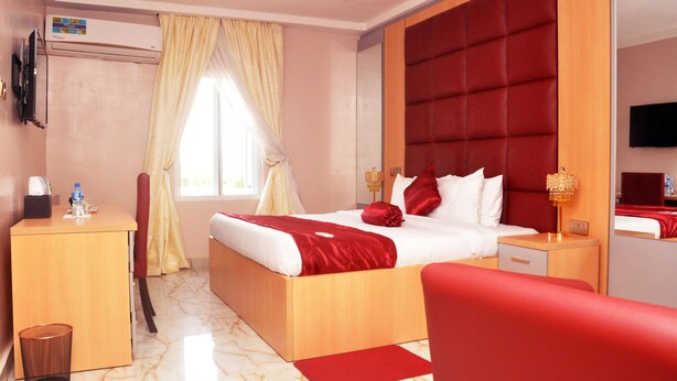 A hotel room with a bed, a desk, a chair, a TV, and an air conditioning unit. - BoardWalk Hotels Zone 5 (Abuja)