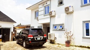 A black SUV parked in front of a white building with blue-framed windows and air conditioning units mounted on the exterior wall. - BoardWalk Hotels Zone 5 (Abuja)