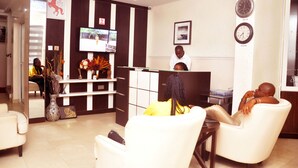 A reception area with a TV, a reception desk, and a seating area with chairs. - BoardWalk Hotels Zone 5 (Abuja)