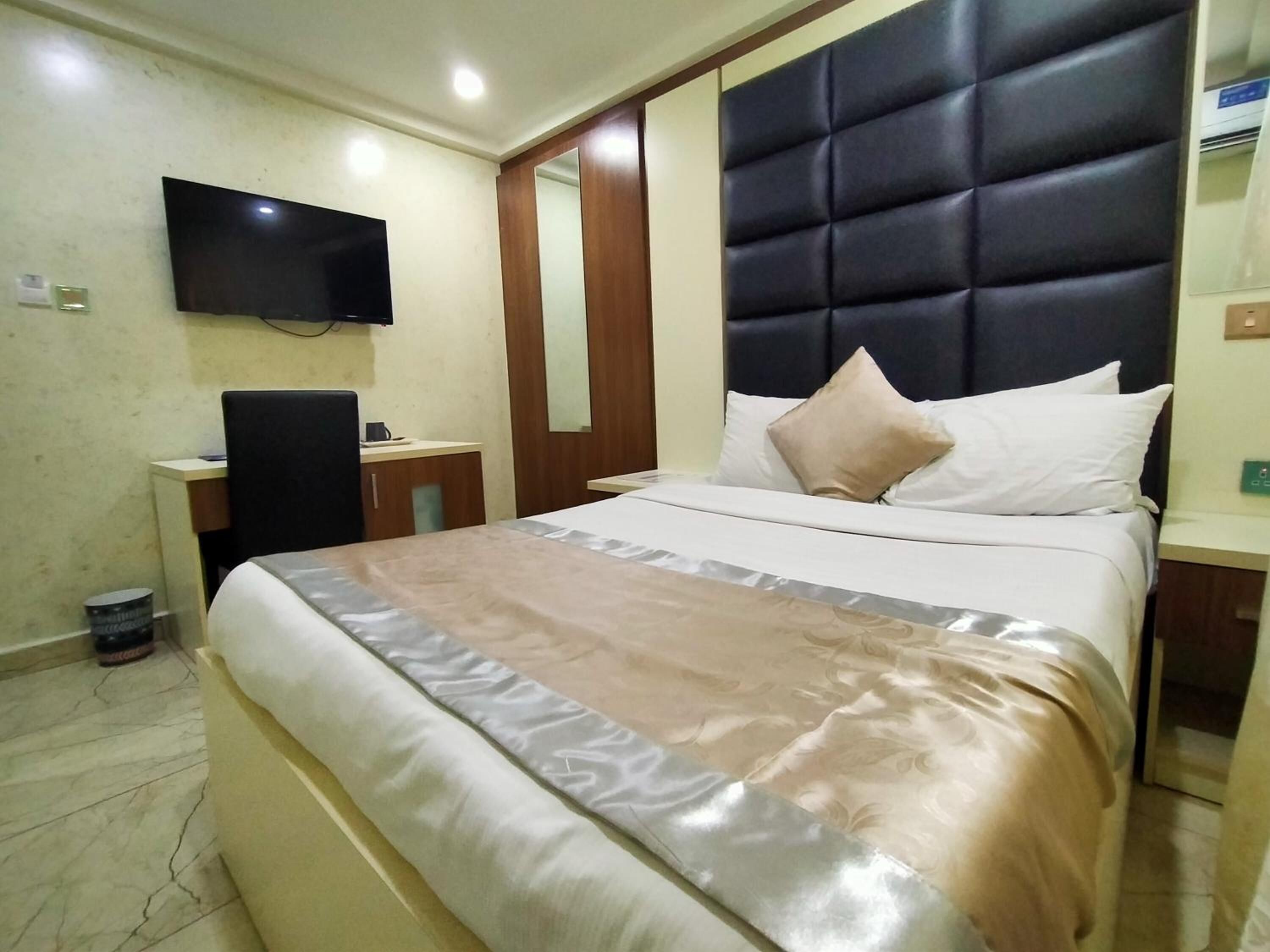 Une chambre d’hôtel comprenant un lit, un téléviseur à écran plat fixé au mur, une table de chevet en bois et un petit bureau avec une chaise.