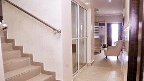 A hallway with a staircase, a sliding glass door, and a seating area with chairs. - BoardWalk Hotels Zone 5 (Abuja)