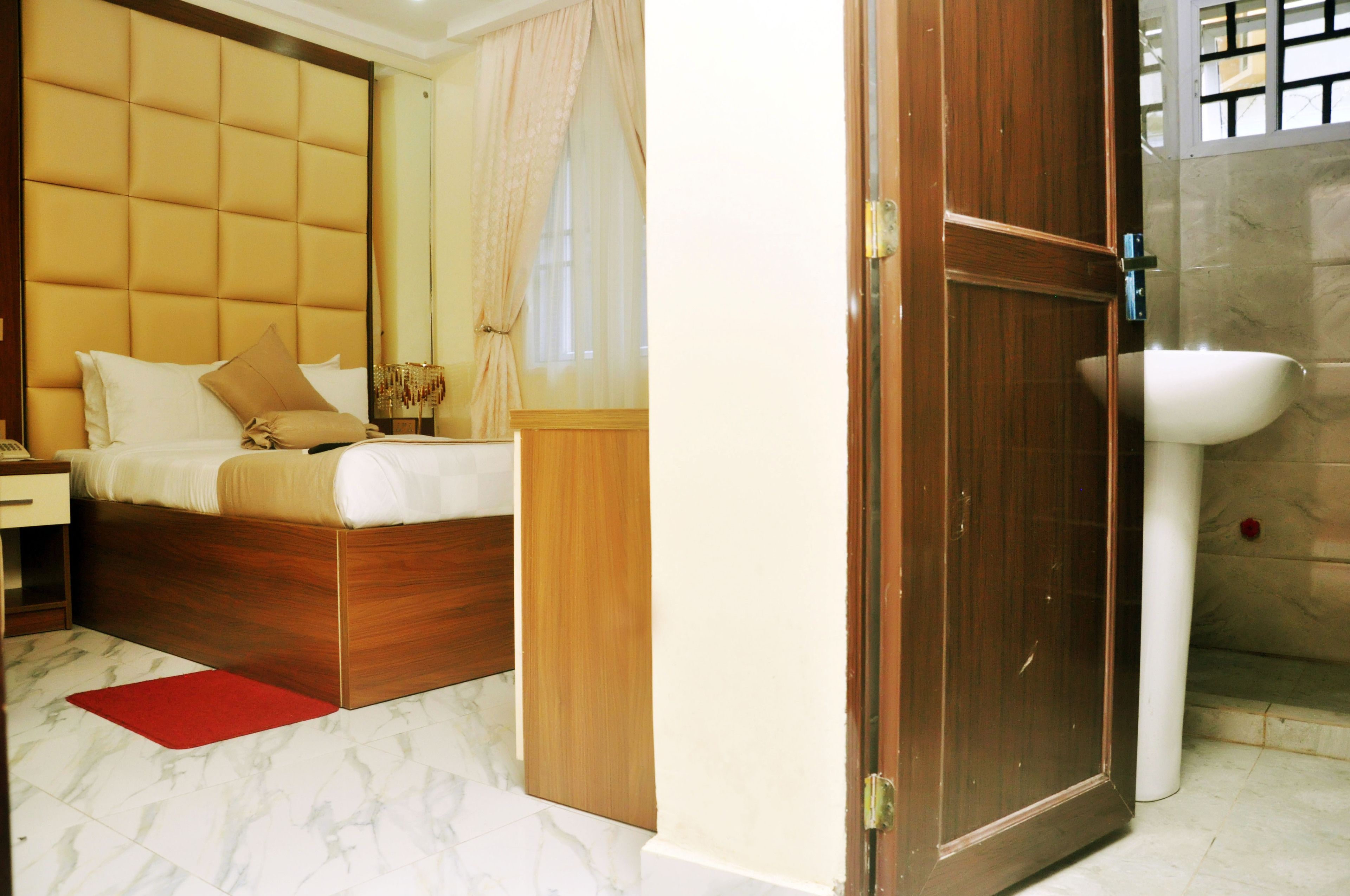 A bedroom with a wooden bed, a nightstand, a red rug, and a bathroom with a sink and shower.