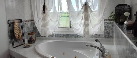 A bathroom with a freestanding bathtub, a window with sheer curtains, and a tiled backsplash.