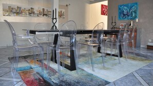 A modern dining area with a glass table and chairs, a colorful rug, and abstract wall art.