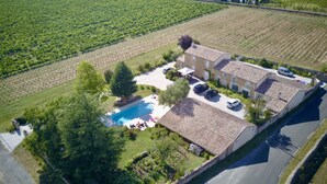 An aerial view of a property with a swimming pool, a stone building, and surrounding vineyards.