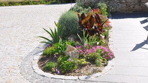 A landscaped garden bed with various plants and flowers, a stone wall, and a cobblestone path.