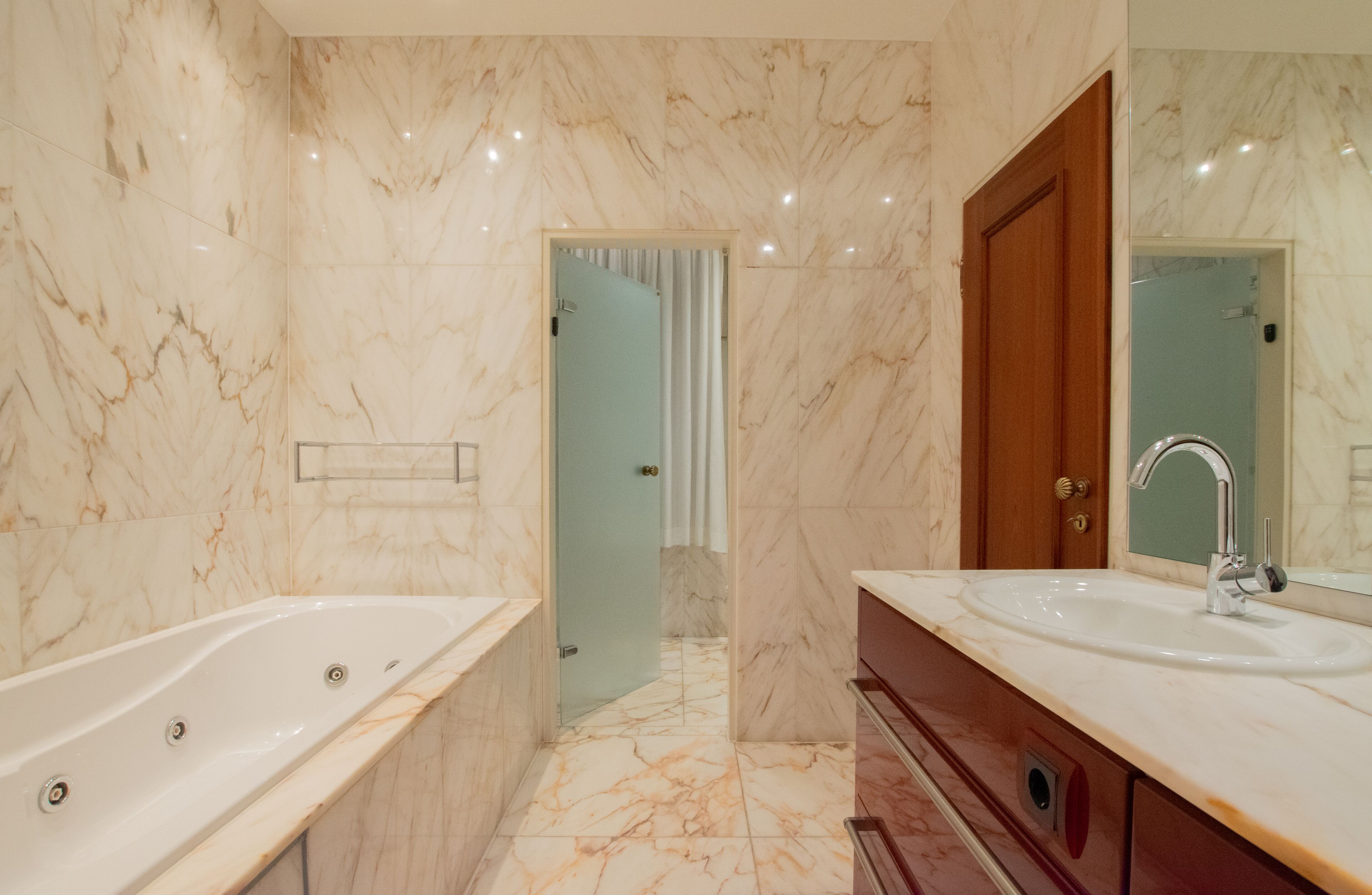 A modern bathroom with a marble floor, a large bathtub, a sink with a mirror, and a wooden cabinet.