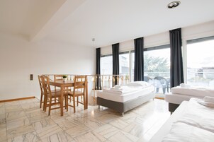 Una habitación de hotel moderna con comedor, cama y ventanas amplias.