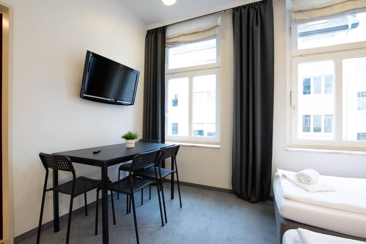 A hotel room with a bed, a TV mounted on the wall, a dining table with chairs, and a window with curtains.