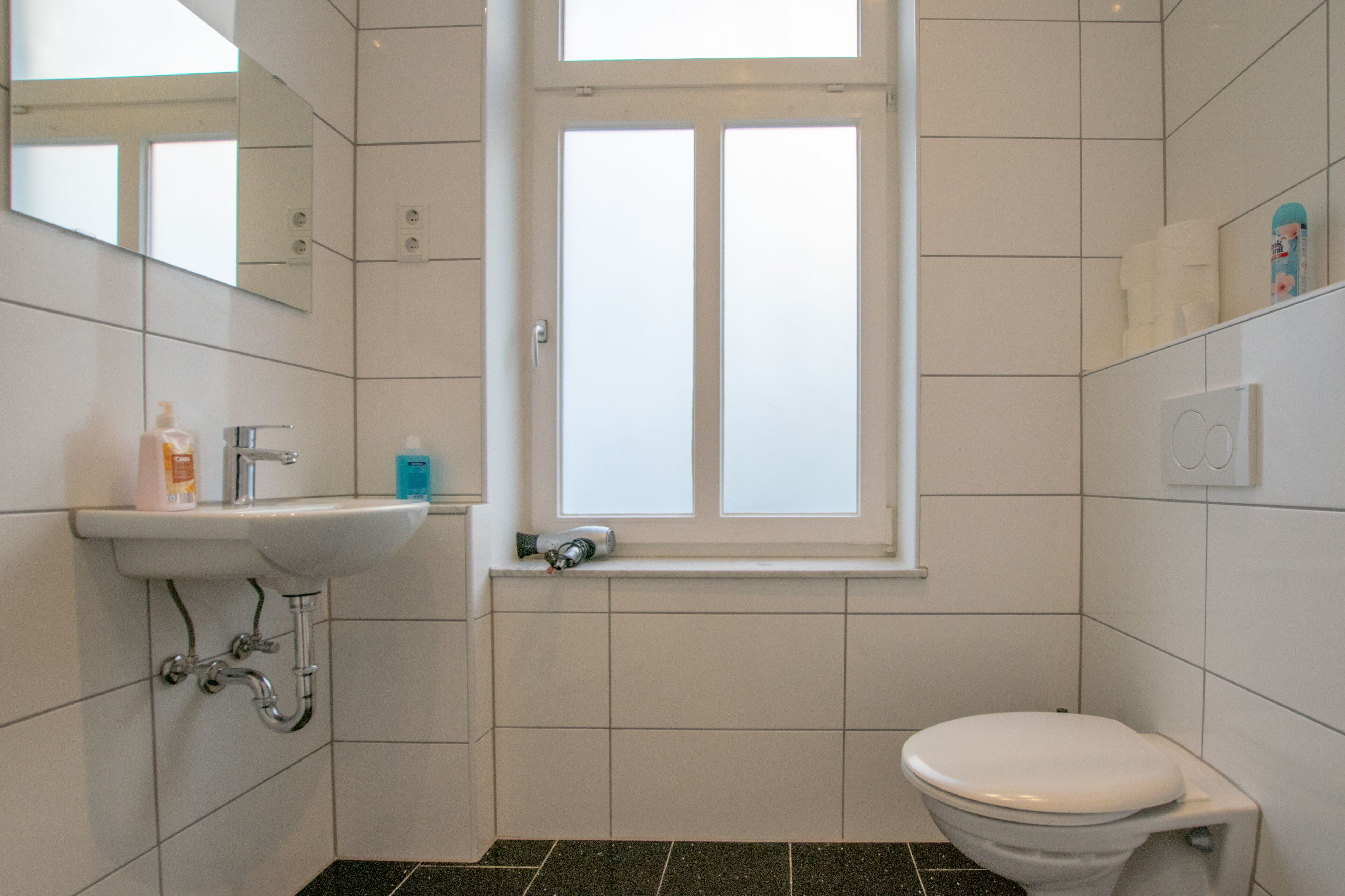 Un bagno con lavandino bianco, uno specchio, una finestra e un water.