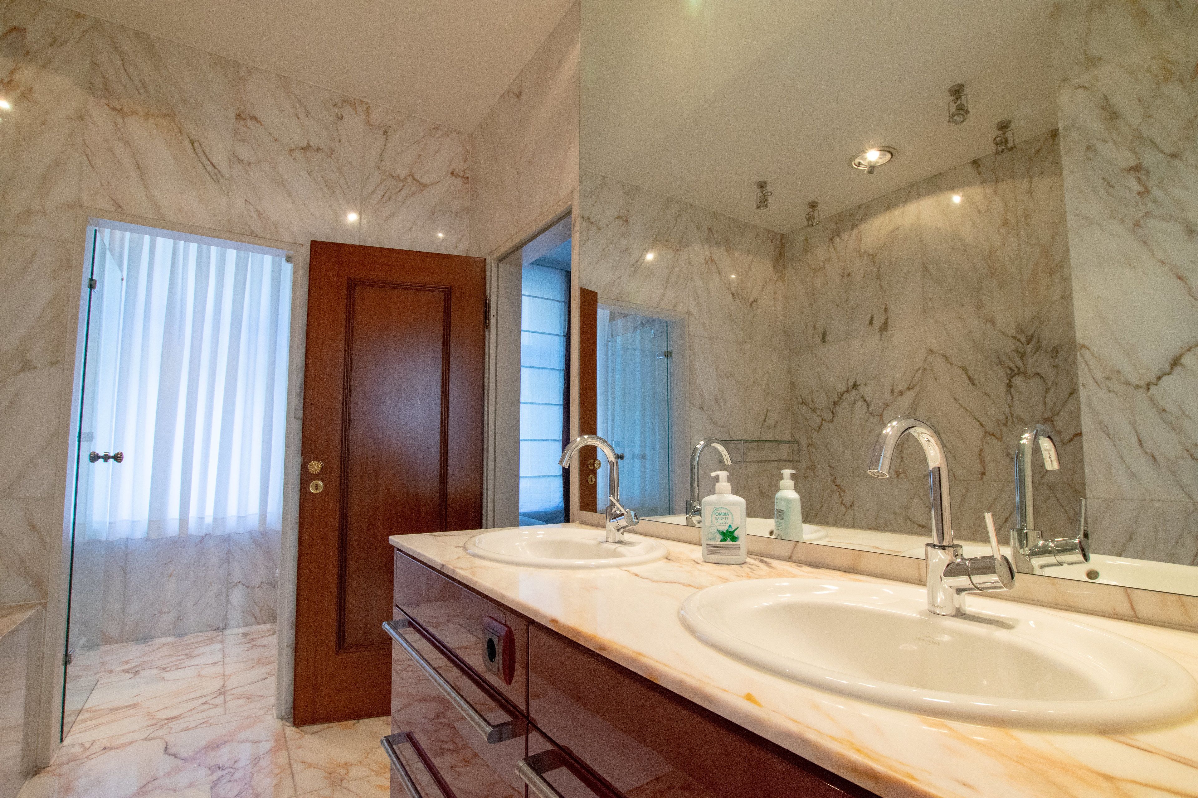 Un baño con dos lavamanos, un espejo grande y paredes de mármol.