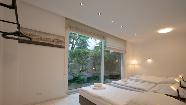 Une chambre d’hôtel moderne avec une grande fenêtre, deux lits et une vue sur la verdure environnante.