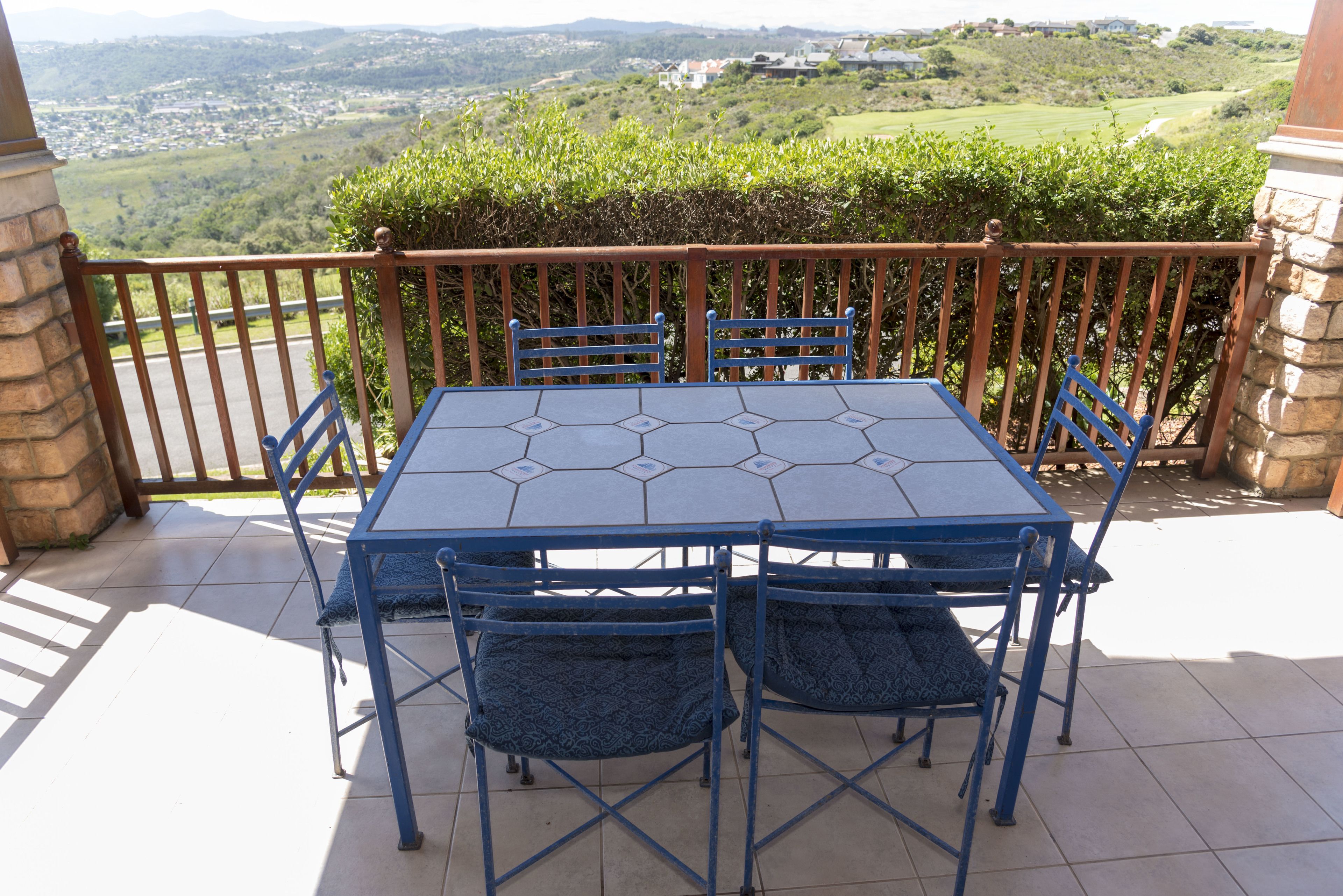 A hexagonal table with blue chairs on a balcony overlooking a scenic landscape.