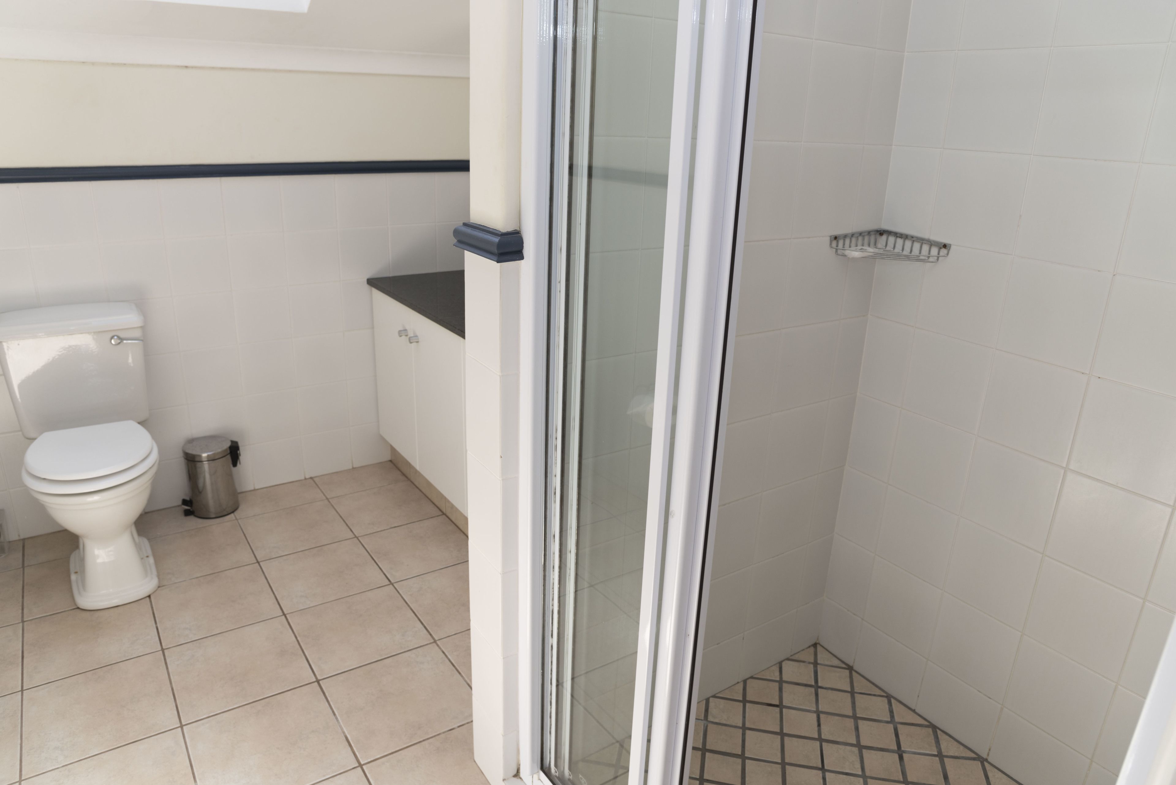 Un bagno con il water, un cestino, una doccia con porta in vetro e un lavandino d'angolo.