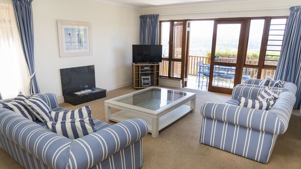 A living room with striped sofas, a glass coffee table, and a TV on a stand. - Villa 10 (Knysna)