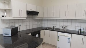 A modern kitchen with white cabinets, a black countertop, a microwave, a dishwasher, and a sink. - Villa 10 (Knysna)