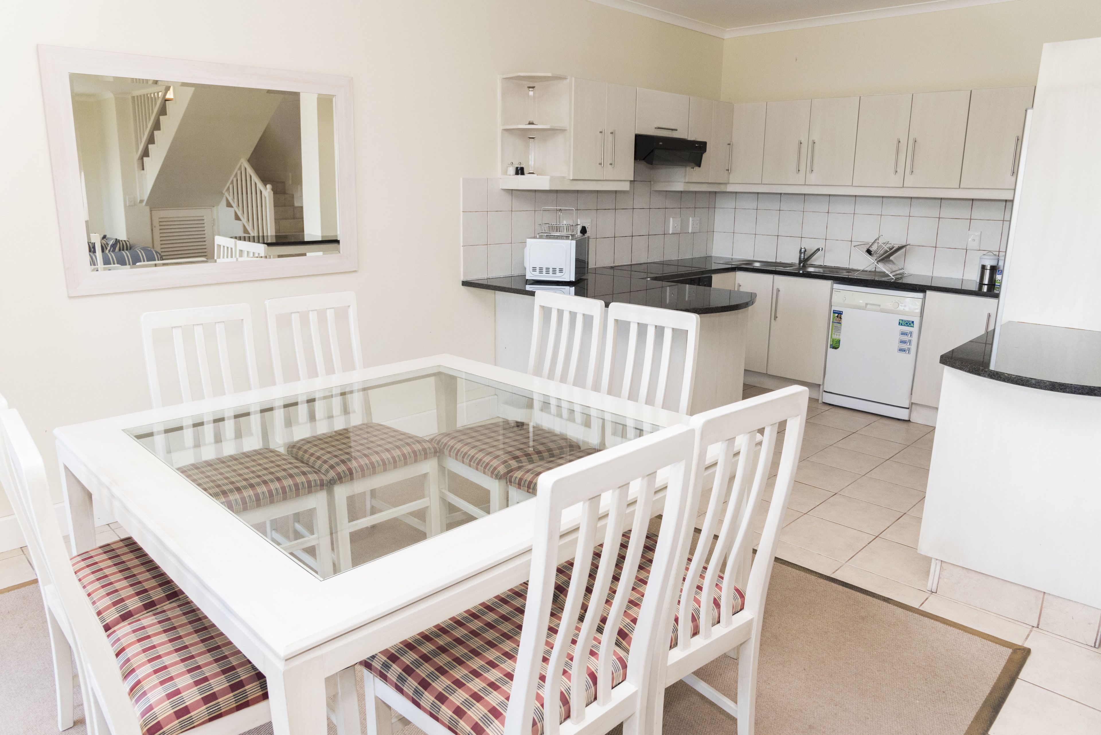 A compact kitchen with white cabinets, a black countertop, and a white dining table with plaid cushions.