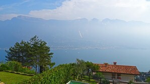 A house with a red-tiled roof, a swimming pool, and a view of a lake with boats and mountains in the background. - Holideal Villa Cinzia (Solofra)