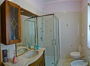 Ein Badezimmer mit zwei Waschbecken, einer Duschkabine aus Glas, einer Toilette und einem Holzkabinet mit Spiegel.