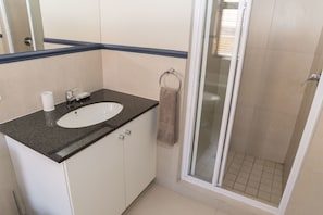 Casa de banho com lavatório, espelho e cabine de duche em vidro.