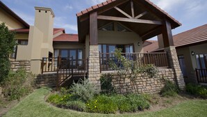 A two-story house with a covered porch, stone foundation, and a red-tiled roof. - Villa 12 (Knysna)