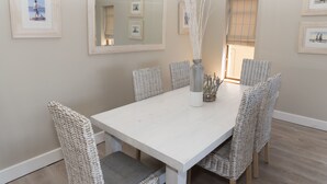 A dining area with a white table and wicker chairs, framed pictures on the wall, and a mirror reflecting the room. - Villa 12 (Knysna)