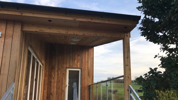 A wooden building with a covered porch, large glass doors, and a metal staircase leading to a balcony. - Godshill Park Barn (Ventnor)