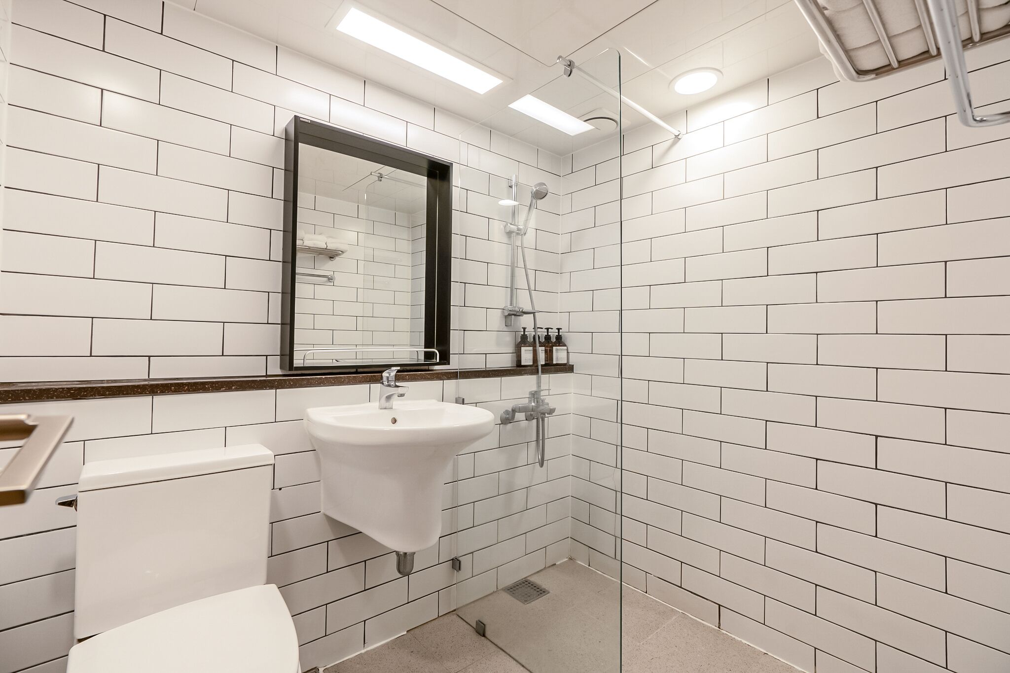 A modern bathroom with white subway tiles, a white sink, a toilet, and a glass-enclosed shower area.