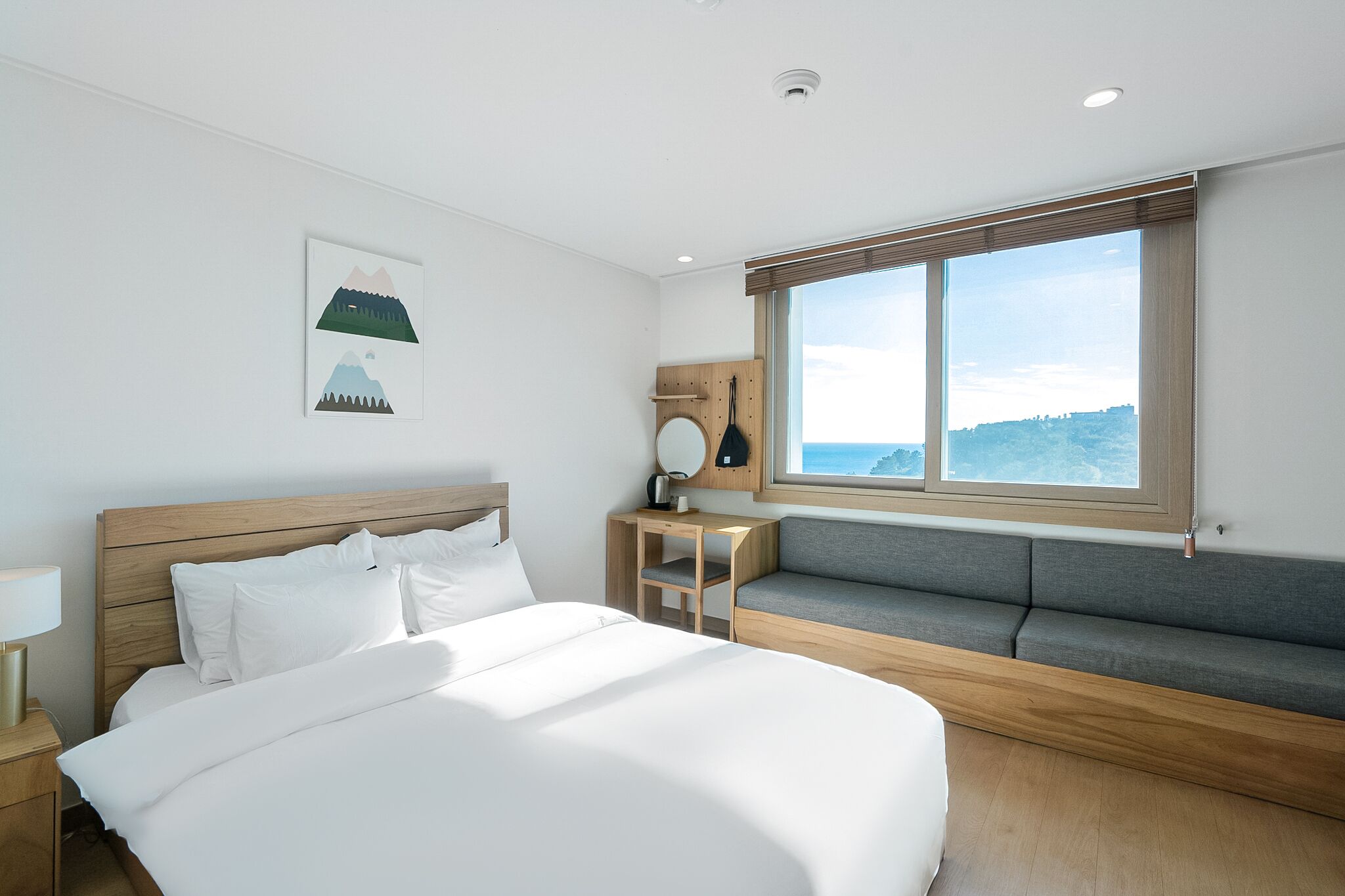 A modern hotel room with a large bed, a seating area, and a view of the sea.