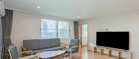 Uma sala de estar moderna com um sofá, cadeiras, uma mesa de centro, uma televisão de tela plana e uma janela com cortinas.
