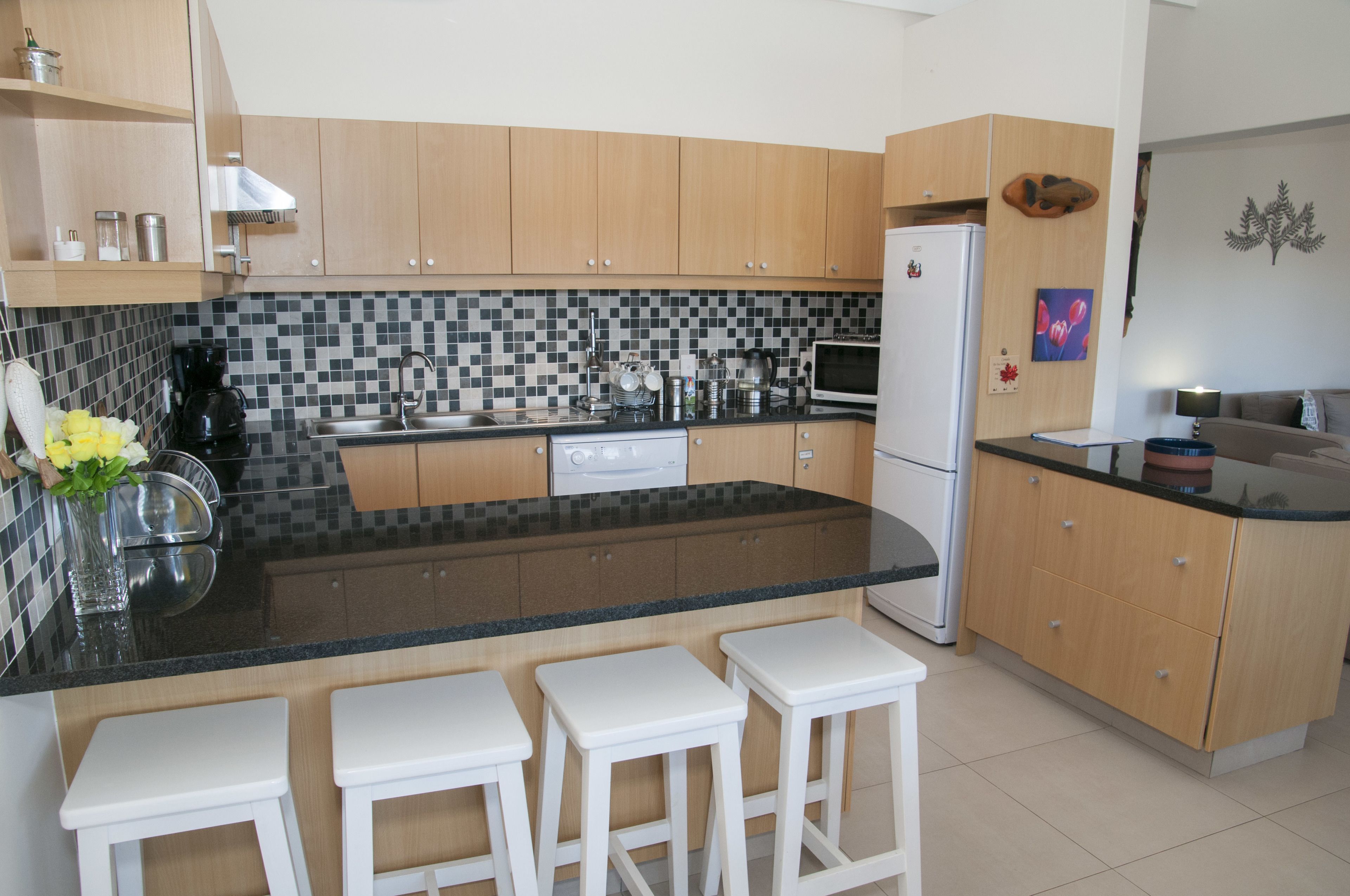 Una cocina moderna con armarios de madera, encimera negra y tres taburetes blancos.